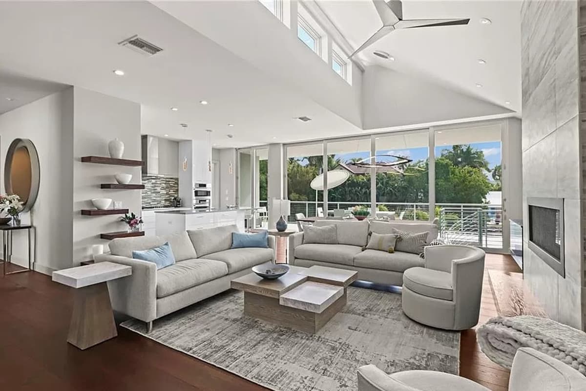 Great room with vaulted ceiling, fireplace, island kitchen, and floor-to-ceiling windows overlooking greenery.
