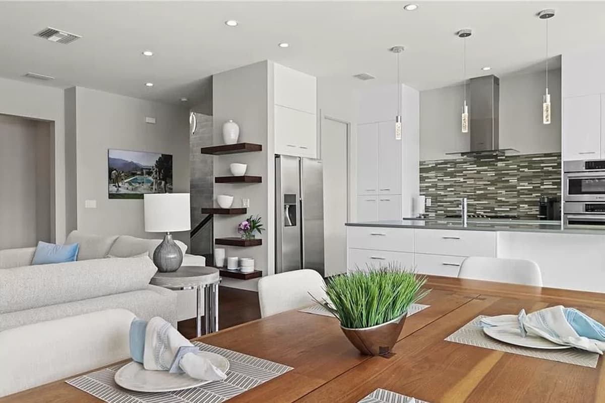Open concept living and kitchen area with island, white cabinetry, stainless steel appliances, and dining table.