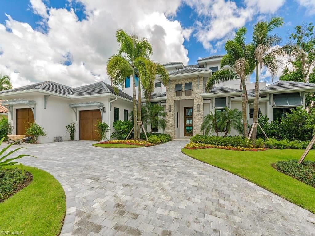 Modern house exterior with multiple rooflines, stone accent facade, dual garage doors, and extensive landscaping.