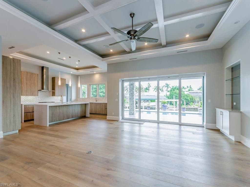 Open concept living area with coffered ceiling, island kitchen, and sliding glass doors leading to an outdoor space.