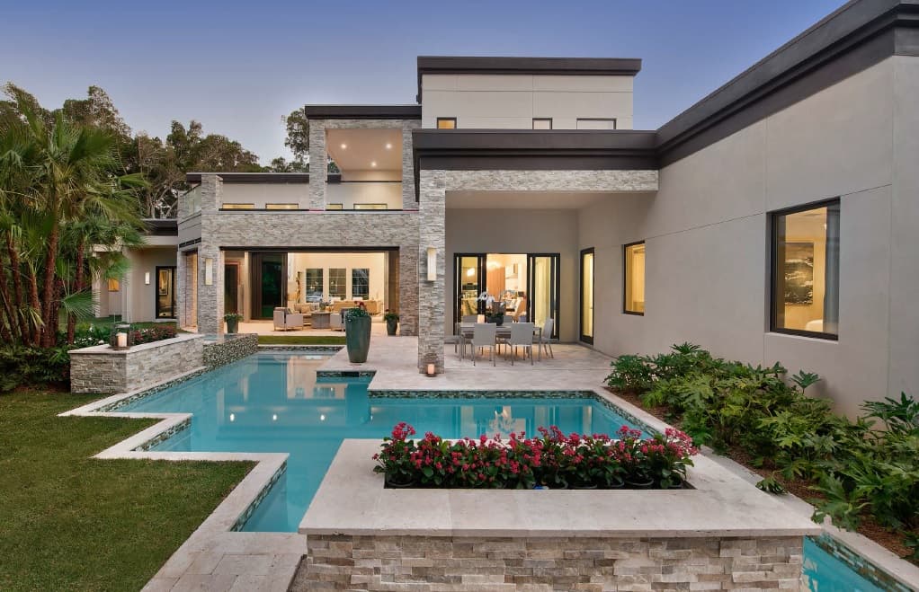 Modern house exterior with geometric pool, multi-level structure, stacked stone accents, and large glass sliding doors.