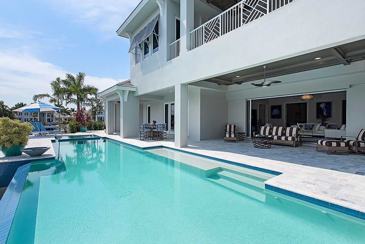 House plan exterior, two stories, with a large pool, covered patio with outdoor seating and large sliding glass doors opening to living area.
