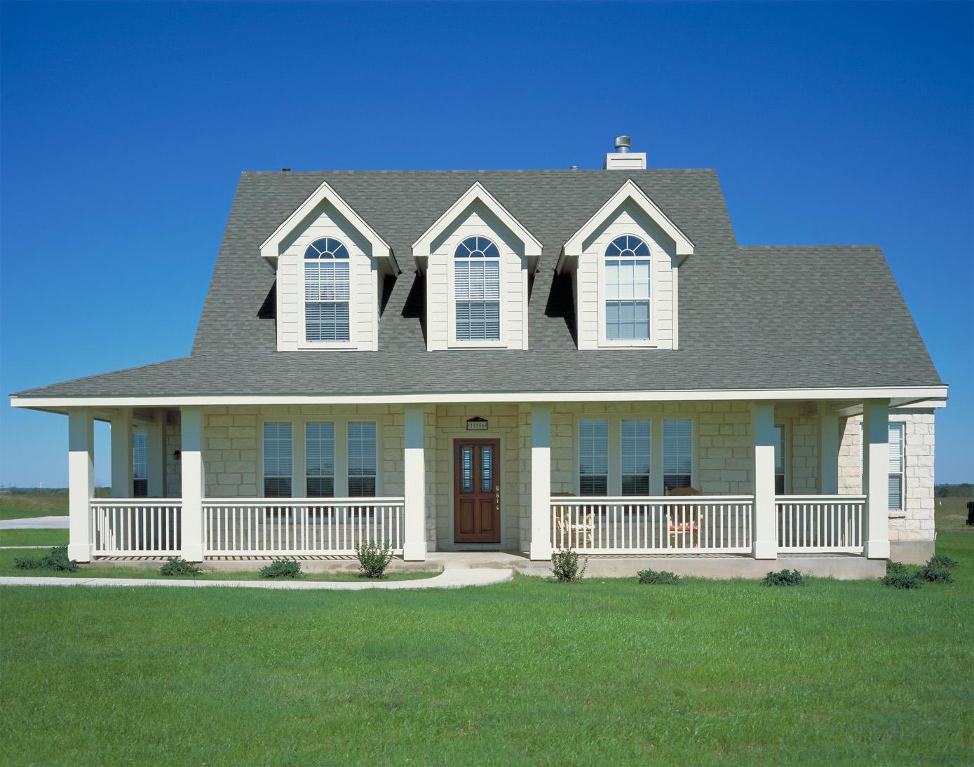 House plan exterior: Two-story house with a wraparound porch, three dormers with arched windows, and stone facade.