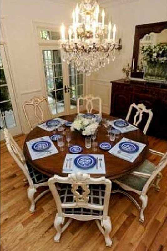 Dining room with round table set for six, crystal chandelier, French doors, and dark wood buffet with mirror.