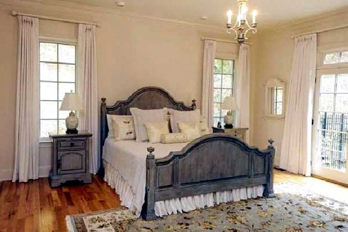 Bedroom with large gray wood bed, two windows with white curtains, bedside table, and chandelier.