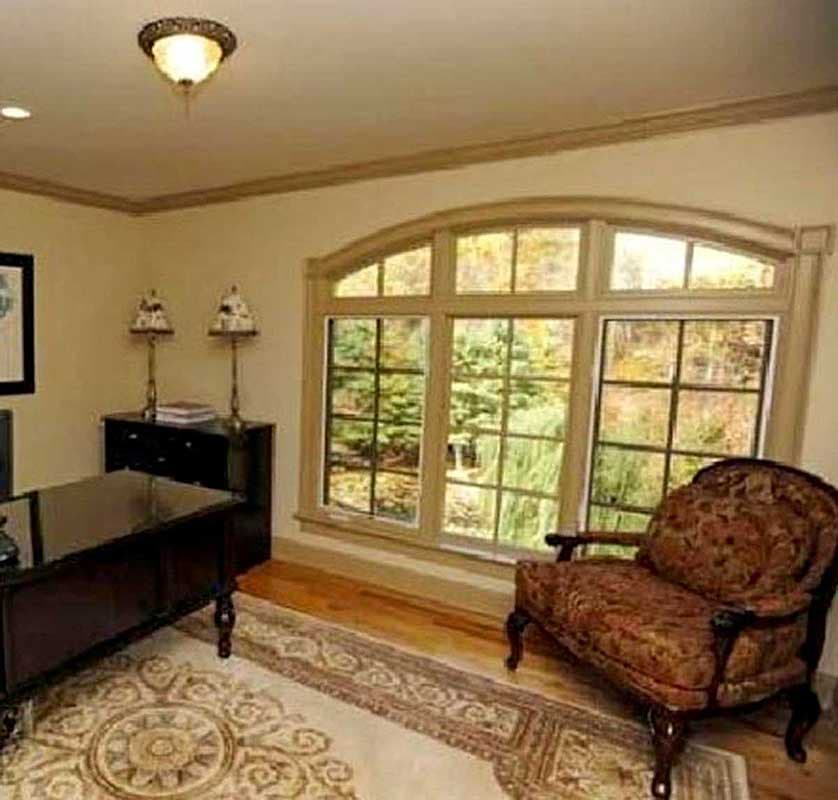 Home office with large arched window, desk, and upholstered chair.