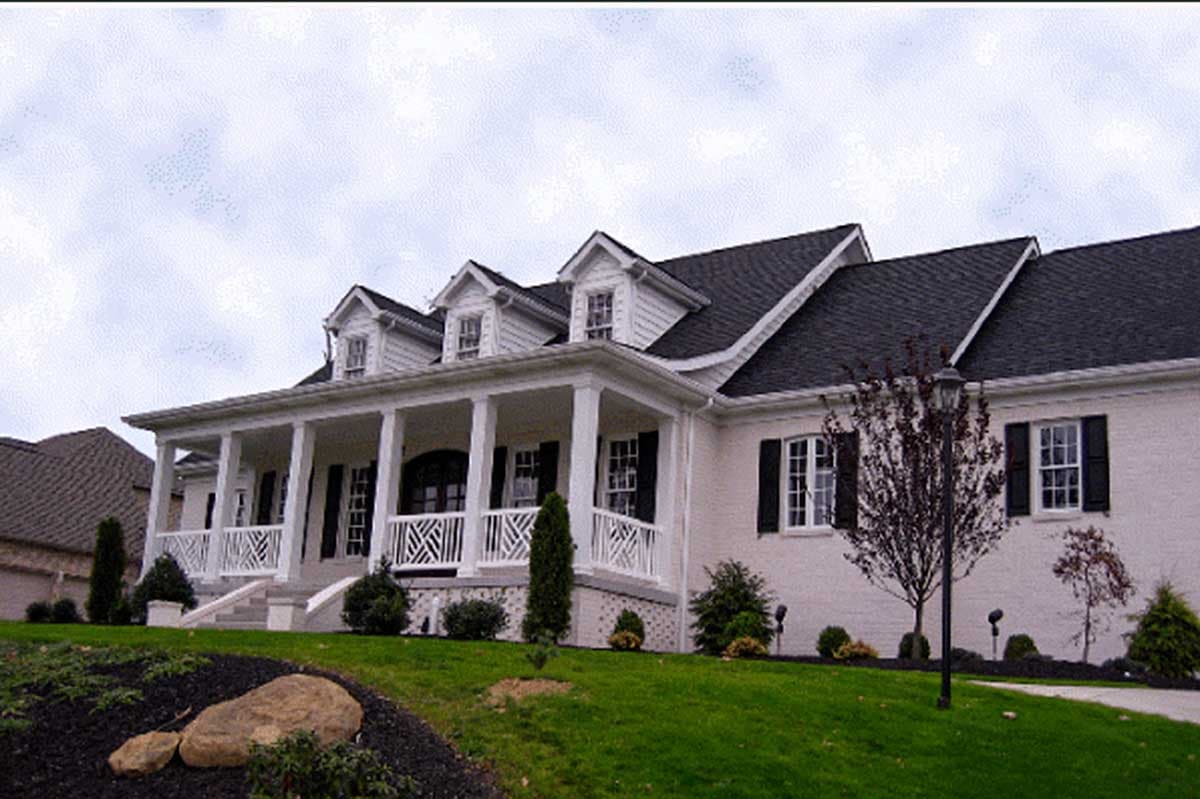 House plan exterior: One-story home with a wraparound porch, multiple gables, dormer windows, and a brick facade.