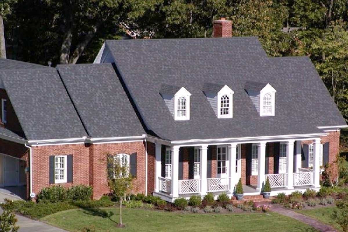 House plan exterior: Red brick, two-story home with a covered porch supported by columns and arched dormer windows.