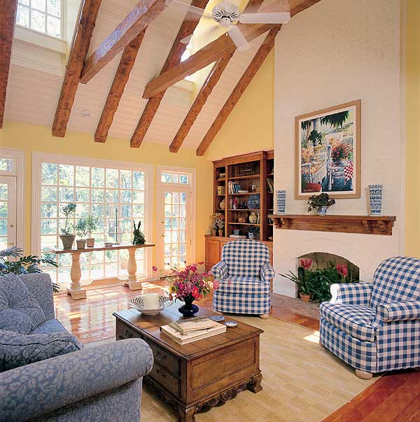 Living room with vaulted ceiling, exposed beams, fireplace, built-in bookshelf, and large windows.
