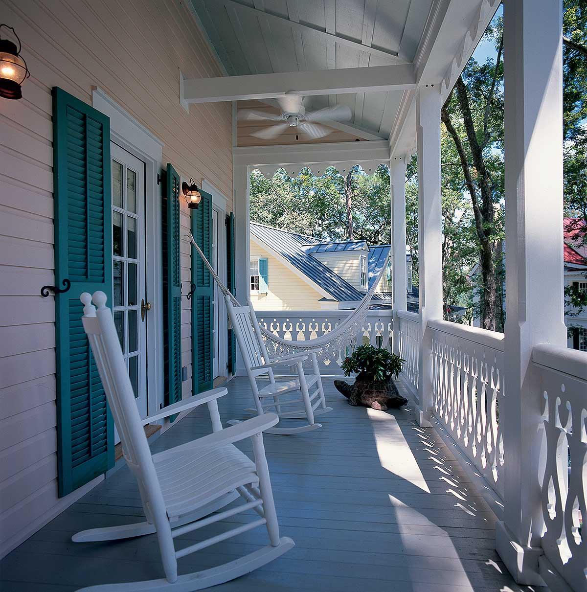 House plan exterior with a wrap-around porch featuring rocking chairs, a hammock, and decorative railings.