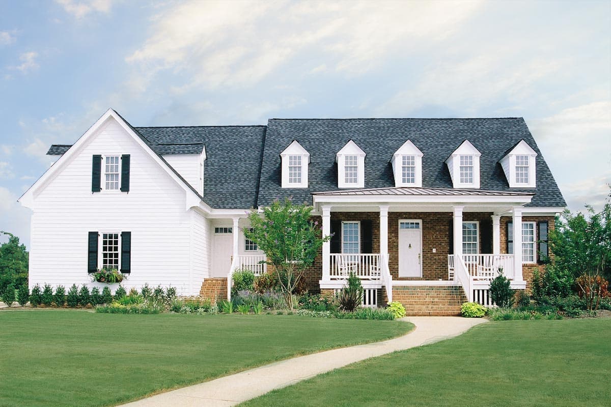 Two-story house plan exterior with white siding, brick accents, prominent gabled dormers, and a deep wrap-around porch.