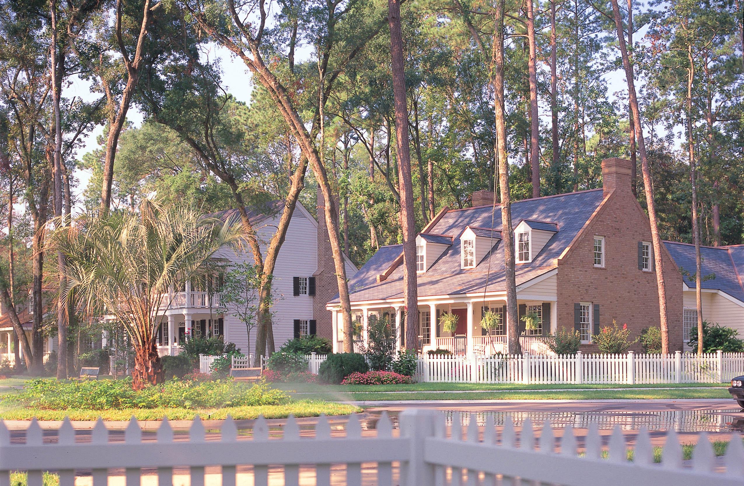 House plan exterior with brick facade, wraparound porch, dormer windows, and picket fence.