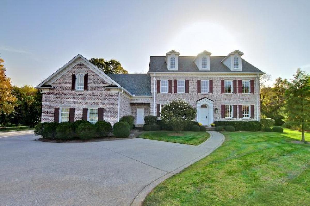 House plan exterior: Two-story brick home with dormers, arched window, shutters, and a central portico.