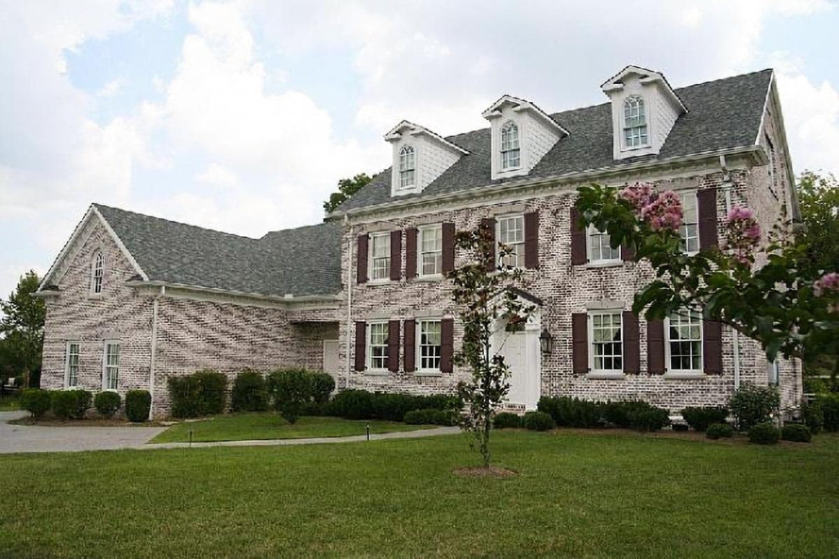 House plan exterior: Two-story brick home with three dormers, shutters, and a prominent gable end with arched window.