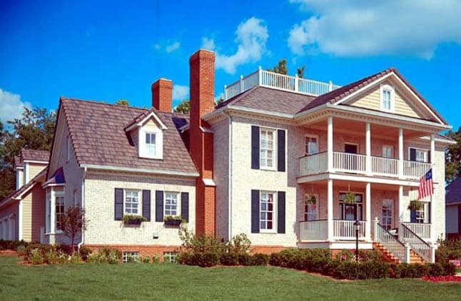House plan exterior: Two-story brick home with a wraparound porch, gabled dormers, and twin chimneys.