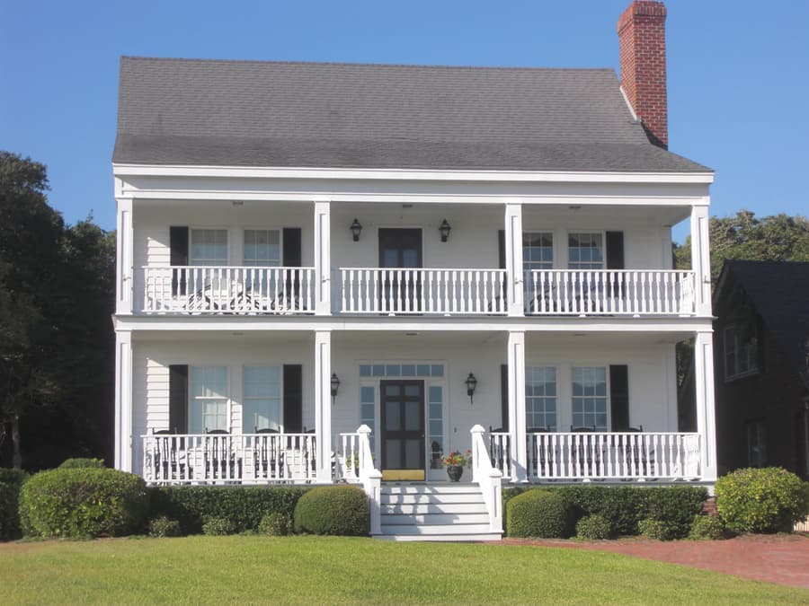 House plan exterior: two-story white home with double porches, red brick chimney, and gabled roof.