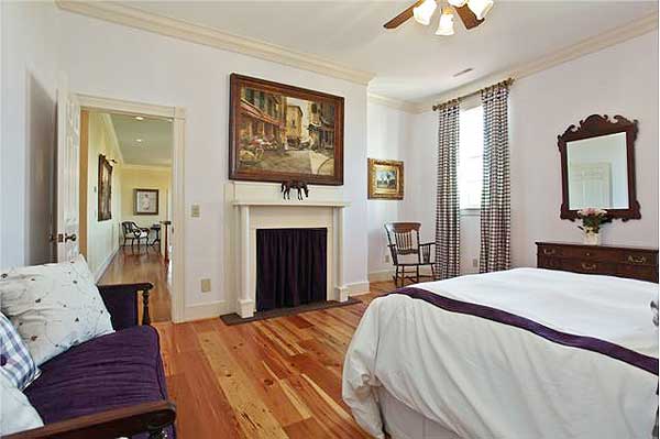Bedroom with fireplace, hardwood floors, ornate mirror, and a purple bench, with an adjoining hallway visible.