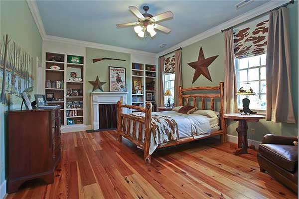 Bedroom interior with rustic log bed, fireplace, built-in bookshelves, and wood plank flooring.