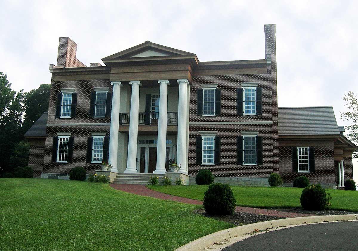 Neoclassical house plan exterior with brick facade, central portico with four columns, symmetrical windows with shutters, and a prominent pediment.