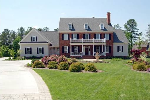 House plan exterior: Two-story brick and siding home with central dormers, a second-story balcony, and a covered front porch.