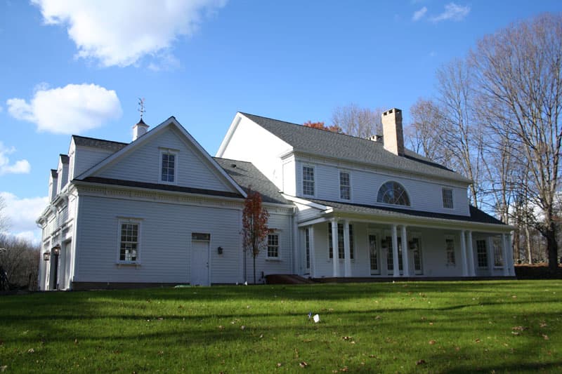 House plan exterior: Two-story white home with gables, dormers, cupola, wide porch with columns, and brick chimney.