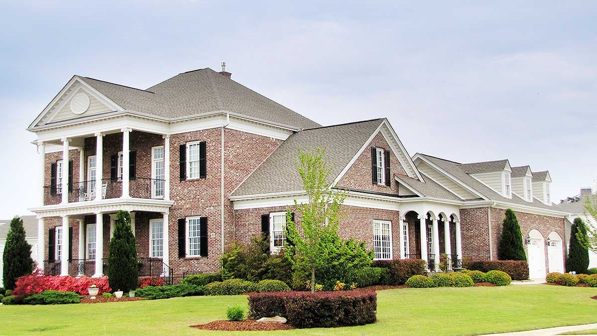 House plan exterior: brick, two-story, central gables, double front porch with columns, multiple dormers, and attached garage.