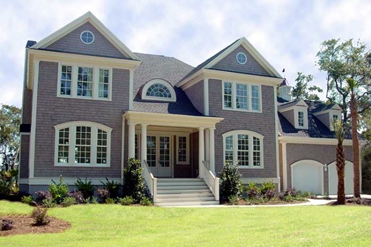 House plan exterior: Two-story home with a covered porch, arched dormers, gables with circular windows, and a side-entry garage.