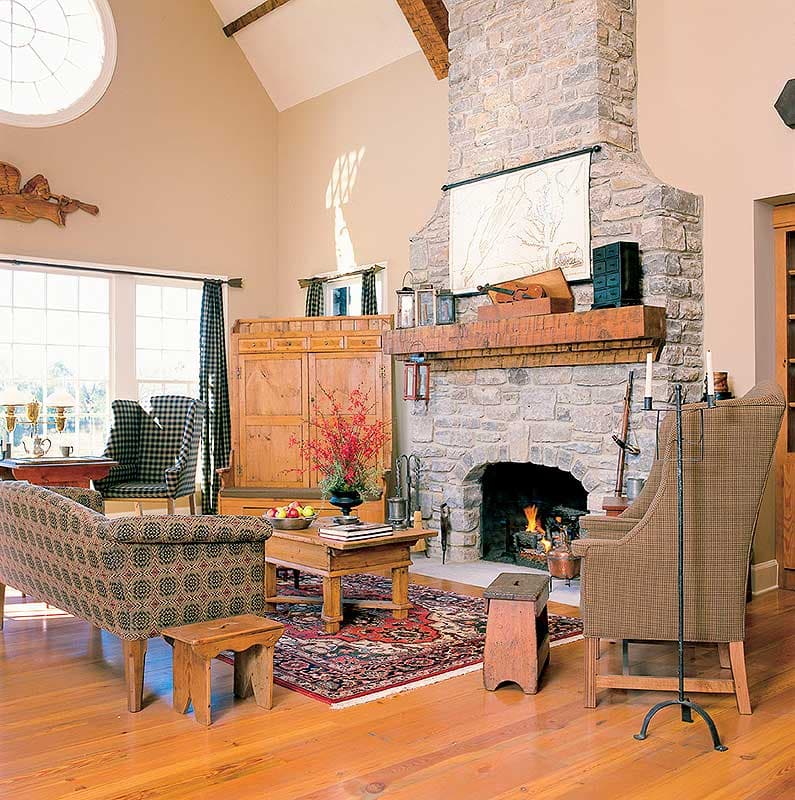 Great room with stone fireplace, vaulted ceiling with exposed beams, large windows, and rustic wooden furniture.