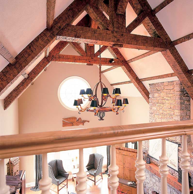 Interior view of a room with a vaulted ceiling, exposed wooden beams, circular window, stone fireplace, and ornate chandelier.