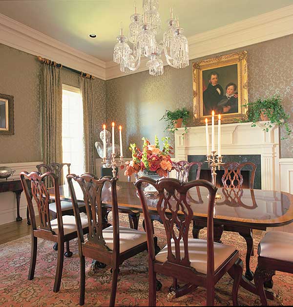 Dining room with oval table, Chippendale chairs, fireplace with portrait, and crystal chandelier.