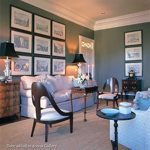 Living room with gallery wall of framed cityscapes above a sofa, flanked by two chairs and a draped side table.