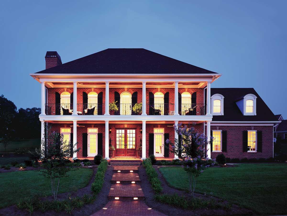 Two-story brick house plan with a central entrance, dual covered porches with columns, arched windows, and dormer windows.