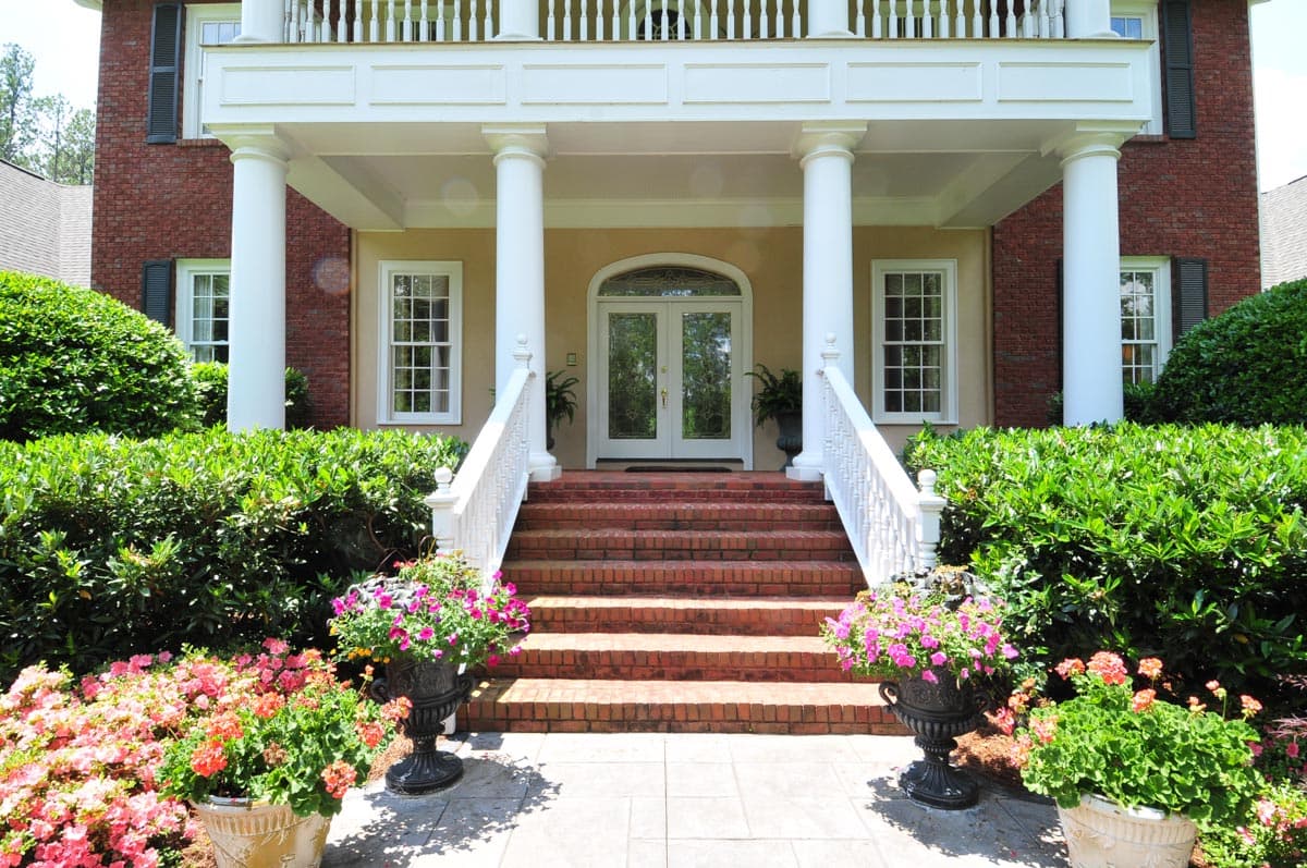 House plan exterior: brick two-story home with a covered porch, white columns, double front doors, and symmetrical windows.