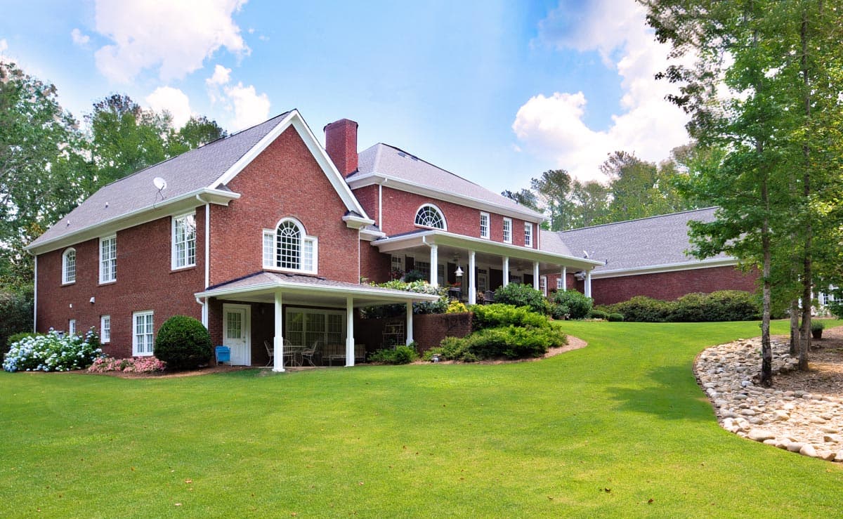 House plan exterior of a two-story brick home with arched windows, a covered porch, and a detached garage wing.