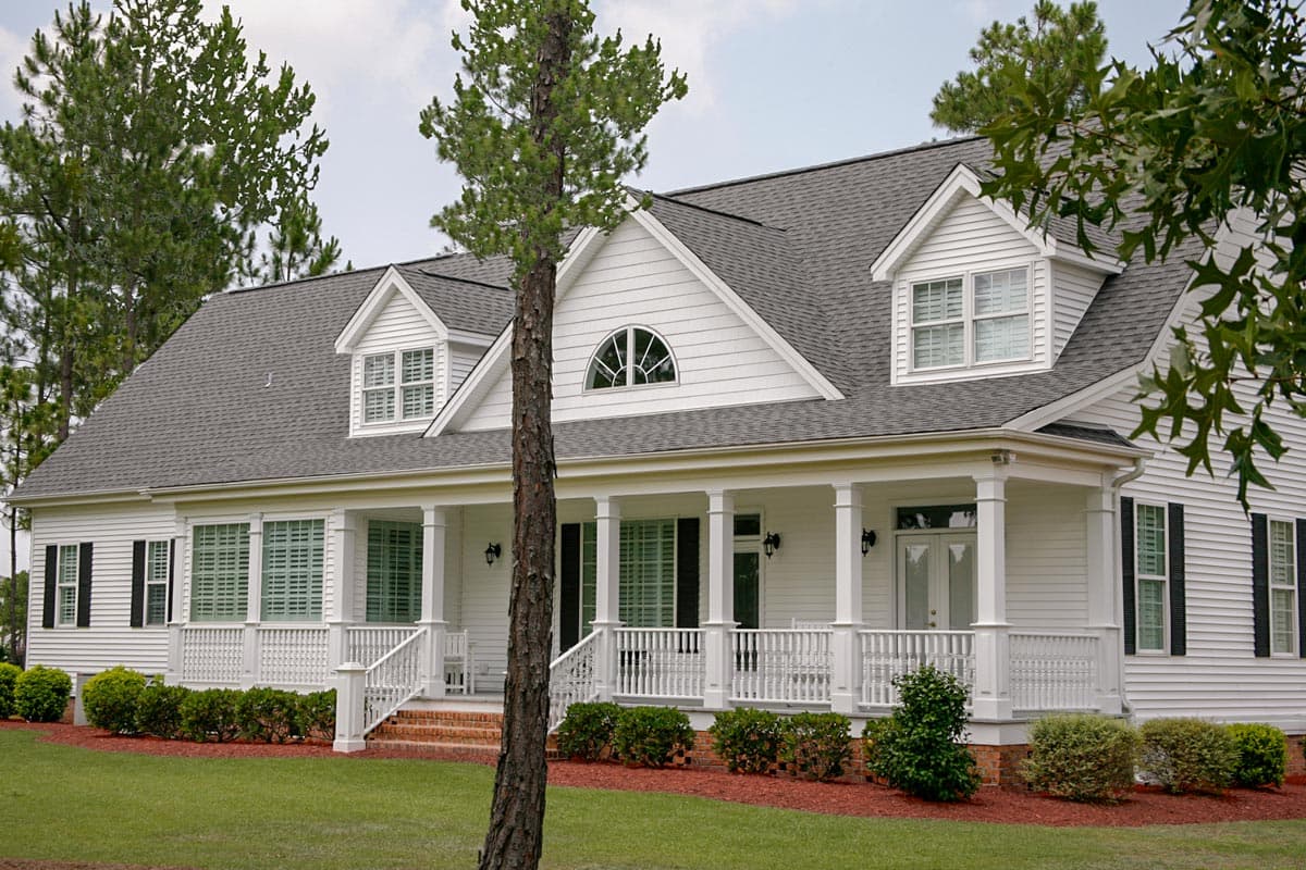 House plan exterior featuring a wraparound porch with columns, dormer windows, and a prominent gable with a fanlight window.