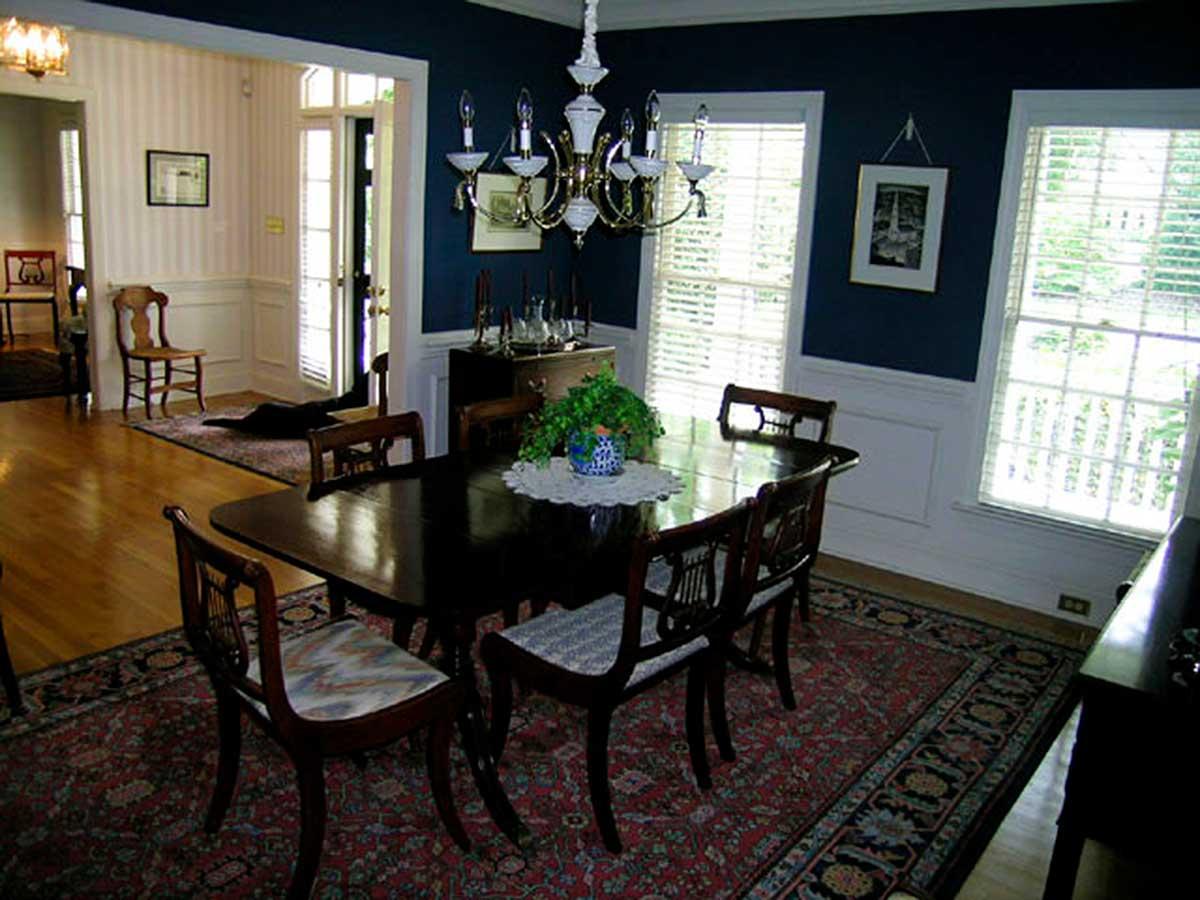 Dining room with dark wood table and chairs, traditional rug, chandelier, and two large windows.