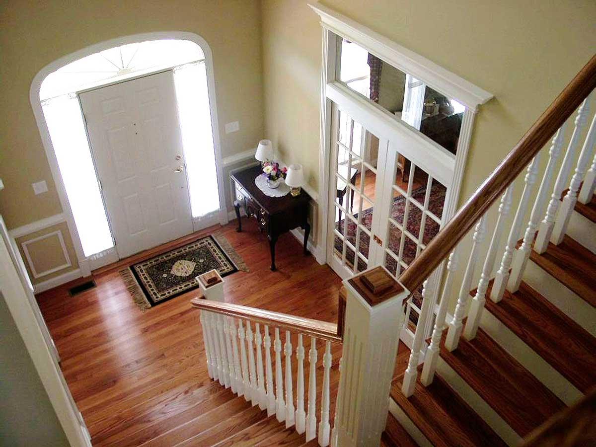 Interior view of foyer with arched entryway, white door, sidelights, paneled wainscoting, rug, console table, and wood staircase with white balusters.
