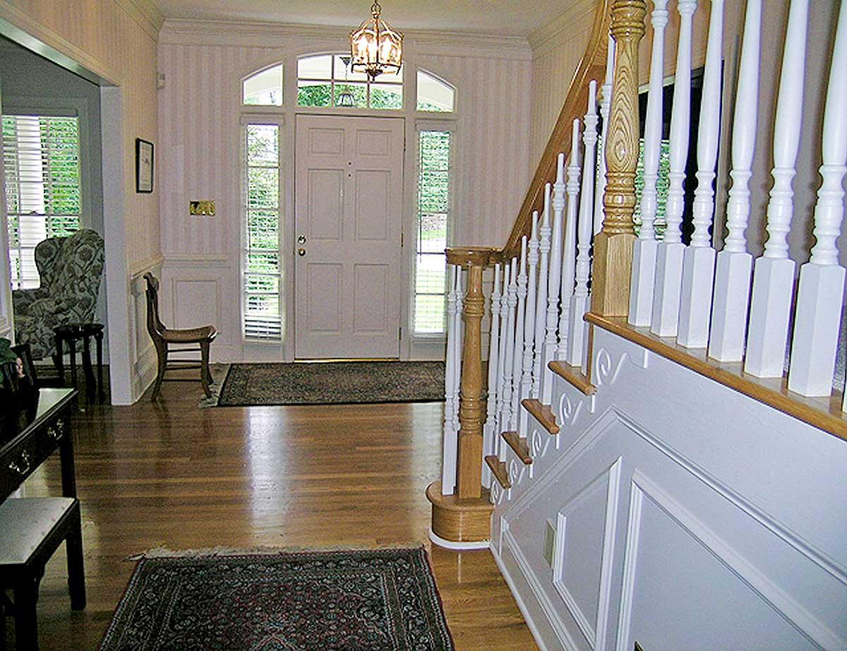 Entryway with double door, arched transom windows, paneled wainscoting, and turned staircase with white balusters.