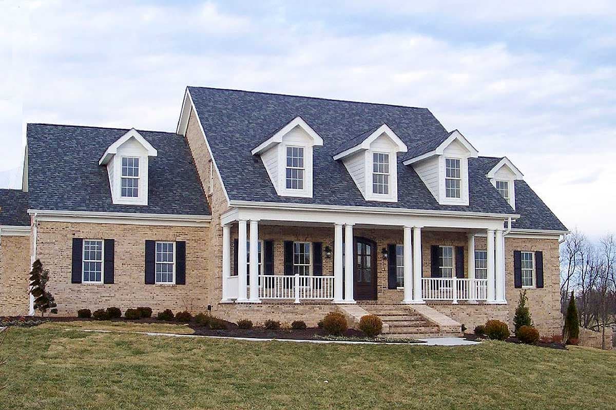 House plan exterior: Brick two-story with a wraparound porch, white columns, and multiple dormer windows.