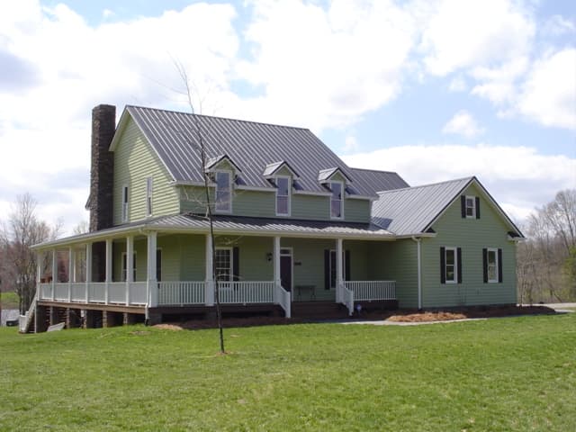 Modern Farmhouse house plan exterior with wraparound porch, prominent stone chimney, and gabled dormers.