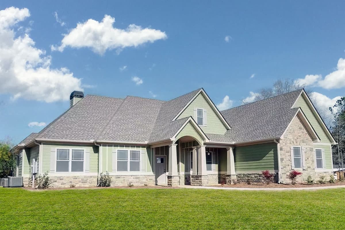 House plan exterior: one-story home with stone accents, covered entry porch, multiple gables, and a prominent chimney.