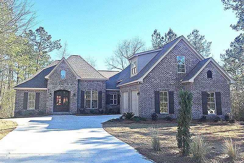 House plan exterior: Brick two-story home with multiple gables, arched entry, dormer window, and attached garage.