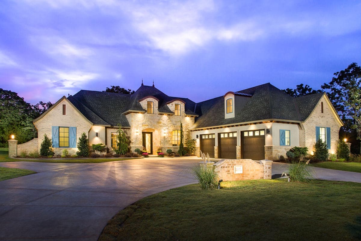 House plan exterior with French Country style, stone accents, multiple gables, dormers, and a three-car garage.