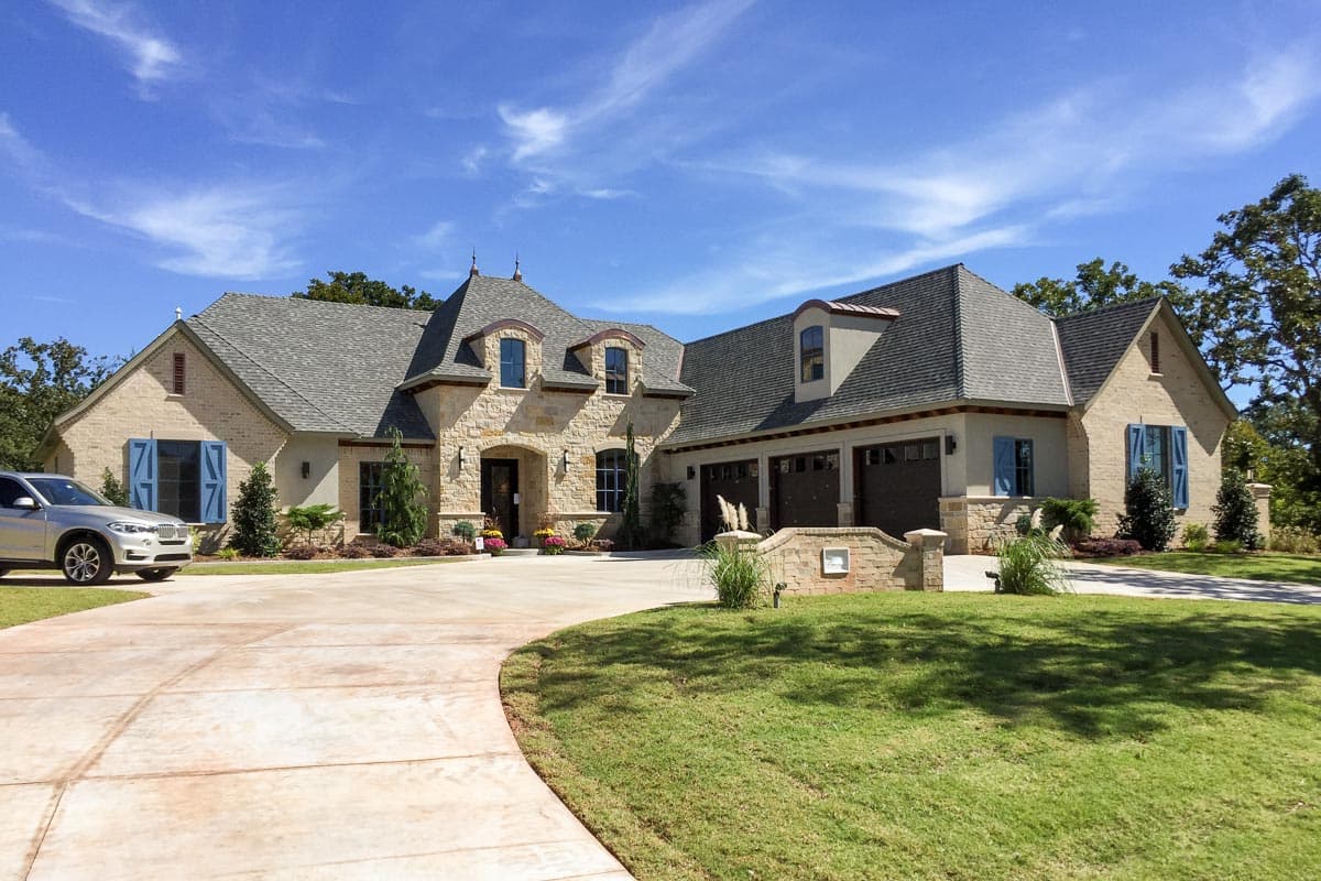 House plan exterior: Two-story French Country style home with stone accents, multi-level rooflines, dormers, and a three-car garage.