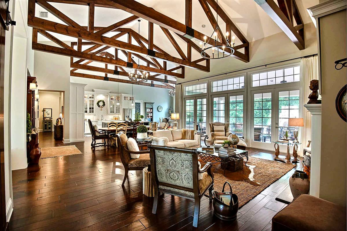 Great room with vaulted ceilings, exposed wood beams, large windows, and an open view to the kitchen and dining area.