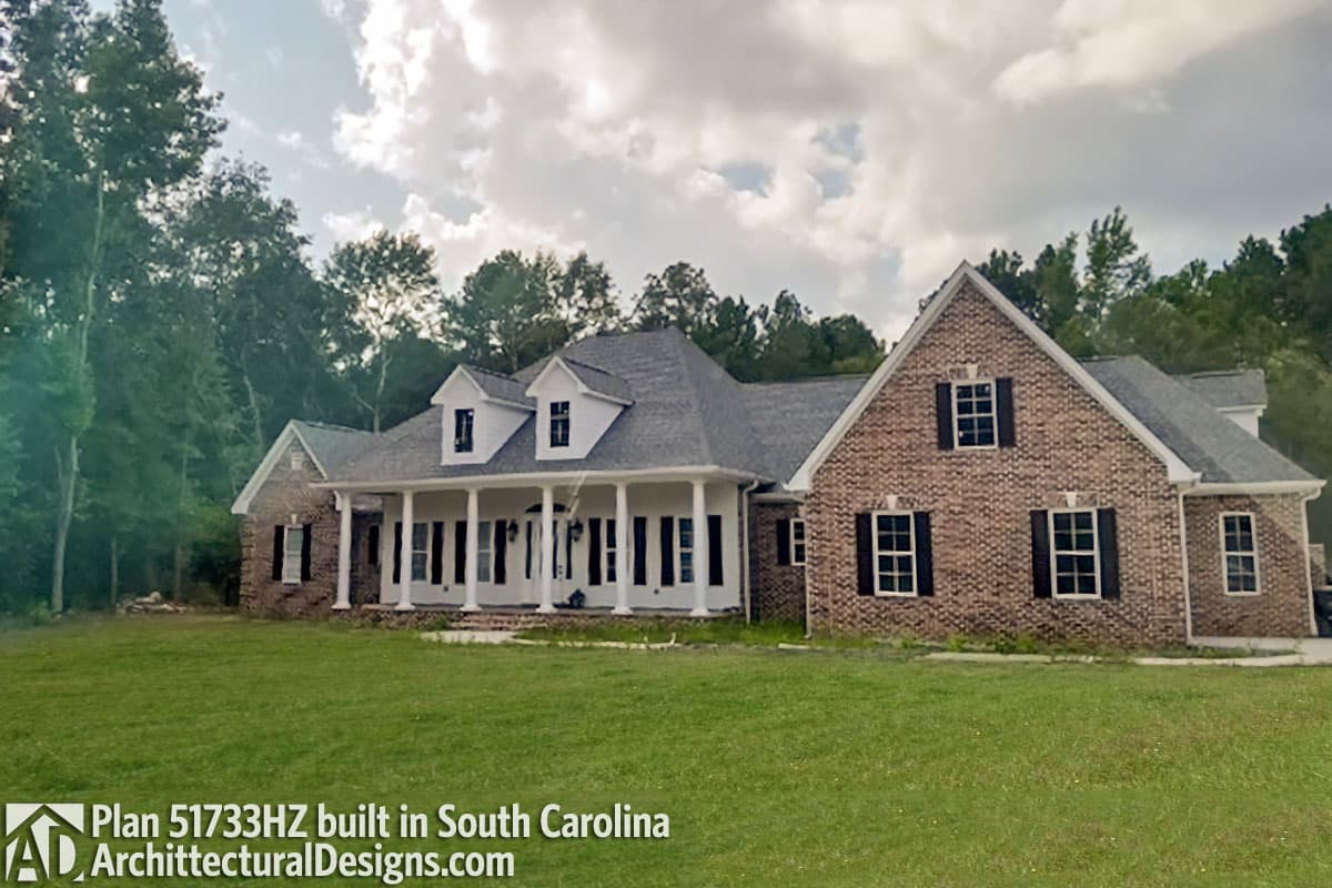 House plan exterior: Brick two-story with wrap-around porch, dormers, and multi-level rooflines.