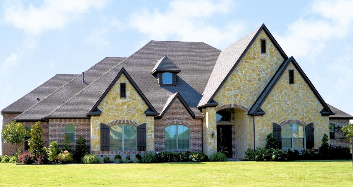 House plan exterior of a two-story home with brick and stone facade, multiple gables, arched windows, and a prominent dormer.