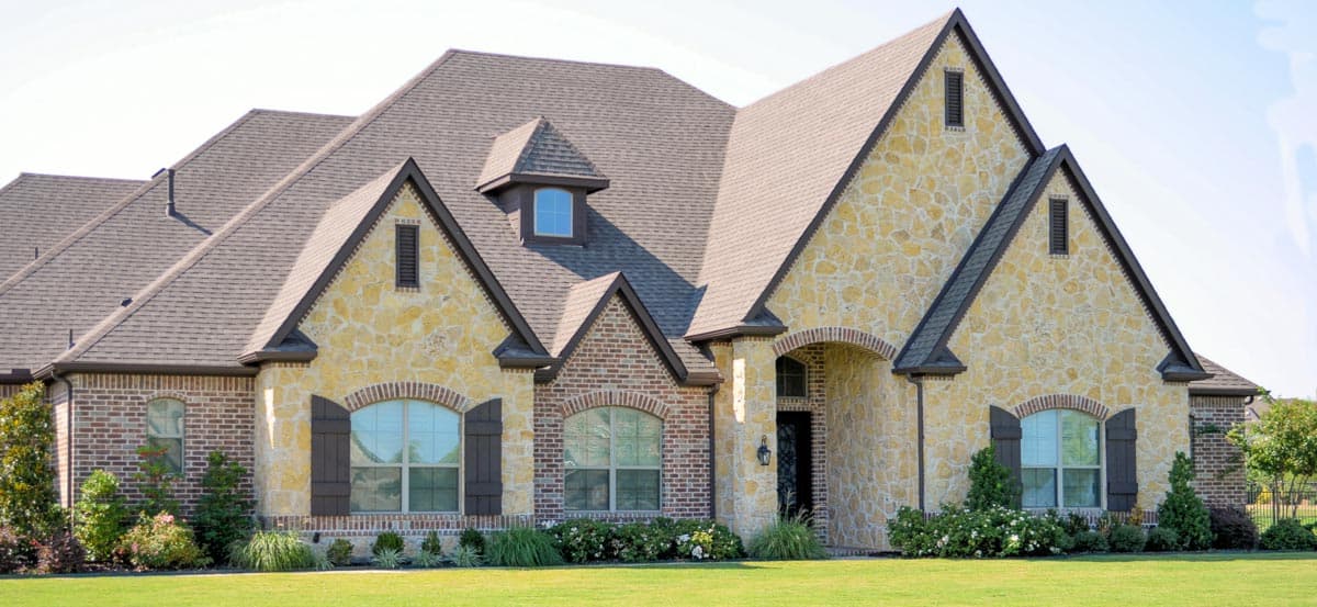 House plan exterior: Two-story home with stone and brick facade, multiple gables, dormer, and arched windows with shutters.