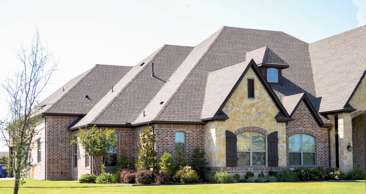House plan exterior featuring brick and stone facade, multiple gables, dormer window, and arched windows.