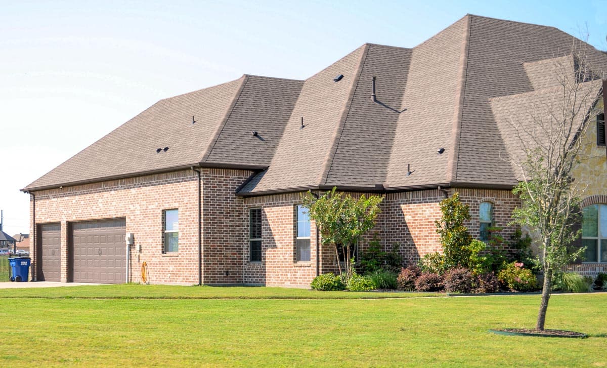 House plan exterior with brick facade, multi-level gabled roof, and three-car garage. Features stone accents and varied window styles.